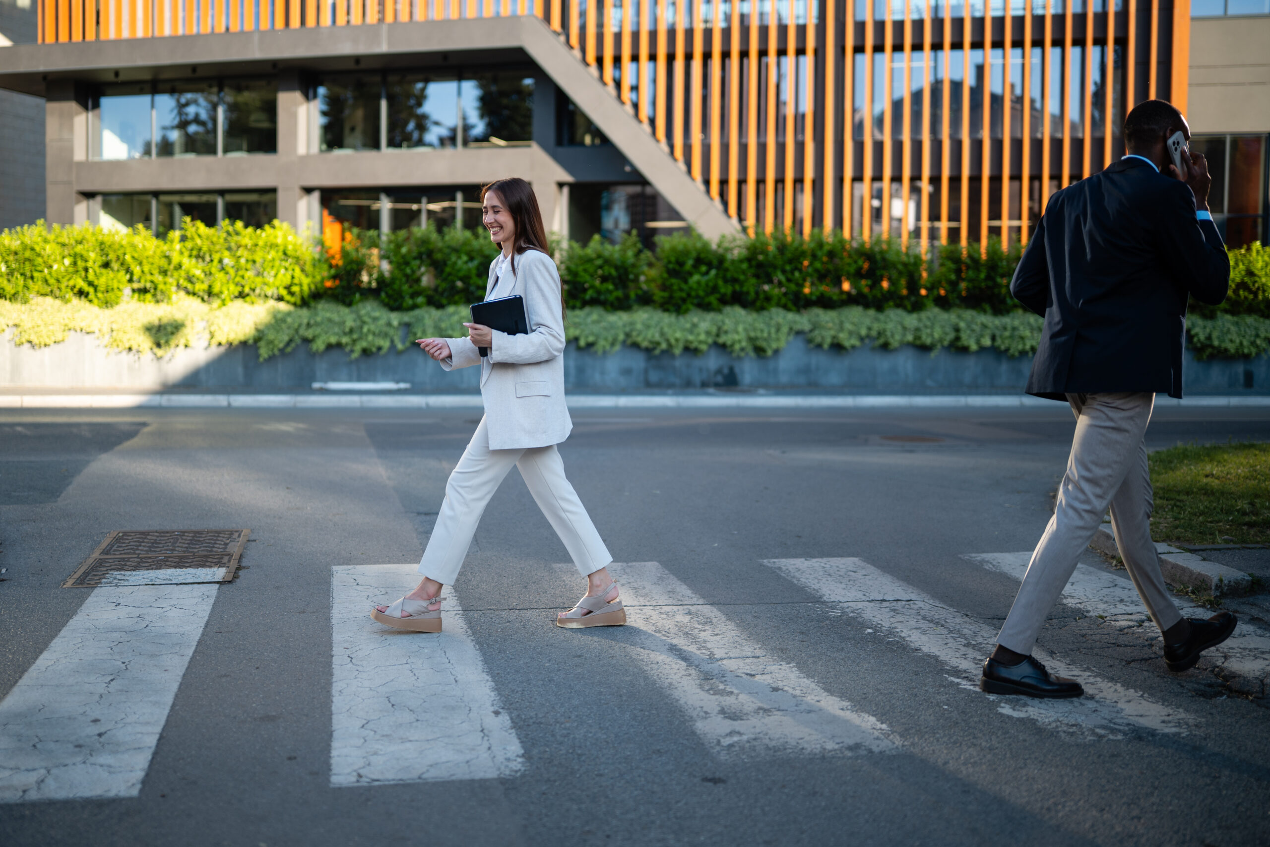 Pedestrian Businesswoman holding a tablet and man talking on phone crossing a zebra crosswalk in an urban environment