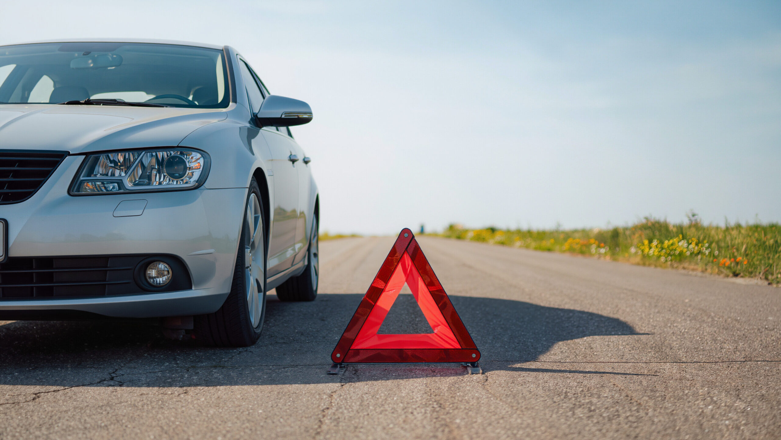 car crash, An orange warning triangle stands on the ground, The vehicle has broken down, It is a typical roadside emergency scene, The car is waiting for a tow truck, Hazard signs are visible