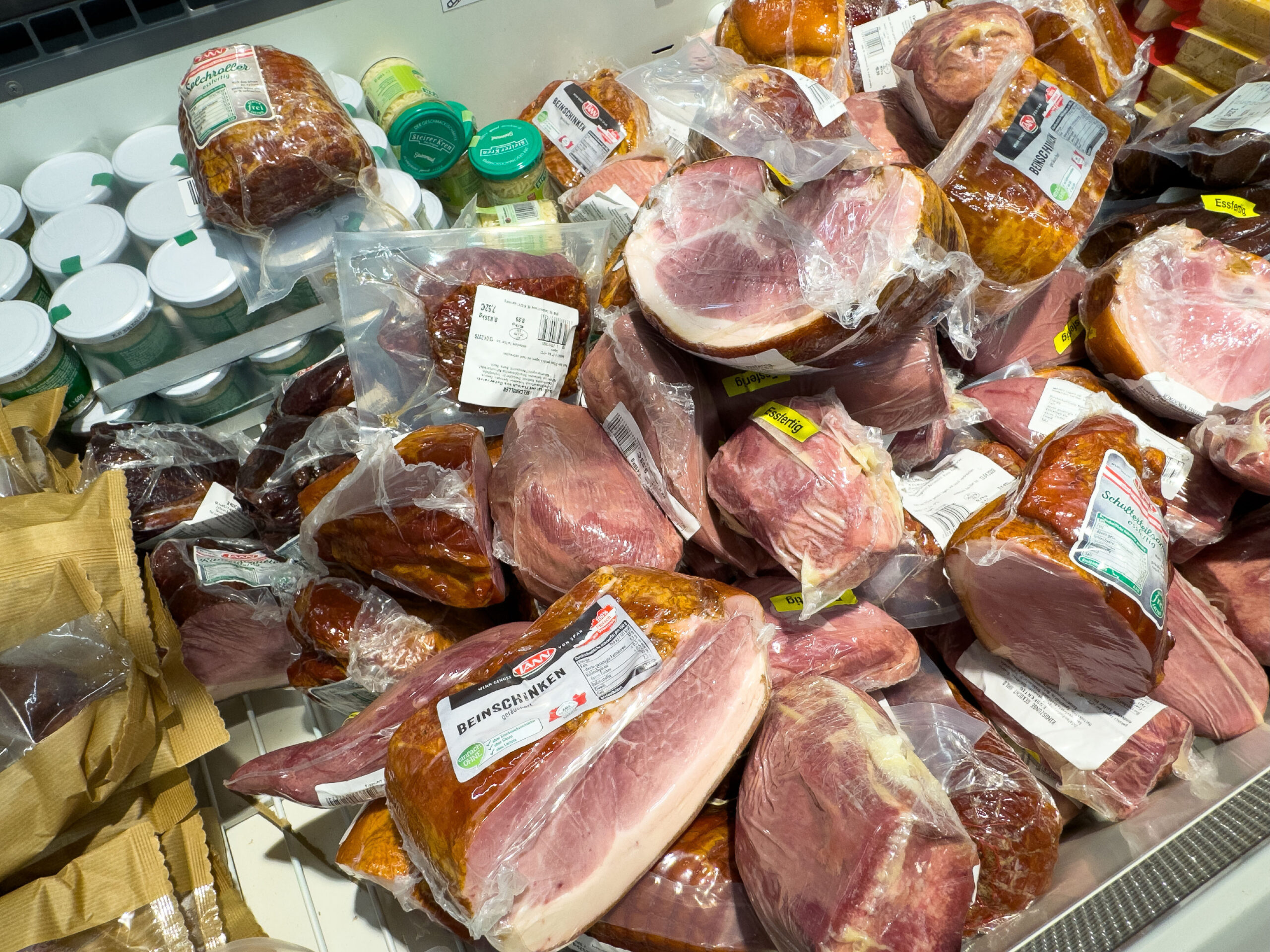 Cooked meat Villach, Austria - March 31, 2026: Various packaged meats, including ham and sausages, are arranged in a grocery store with jars of condiments in the background