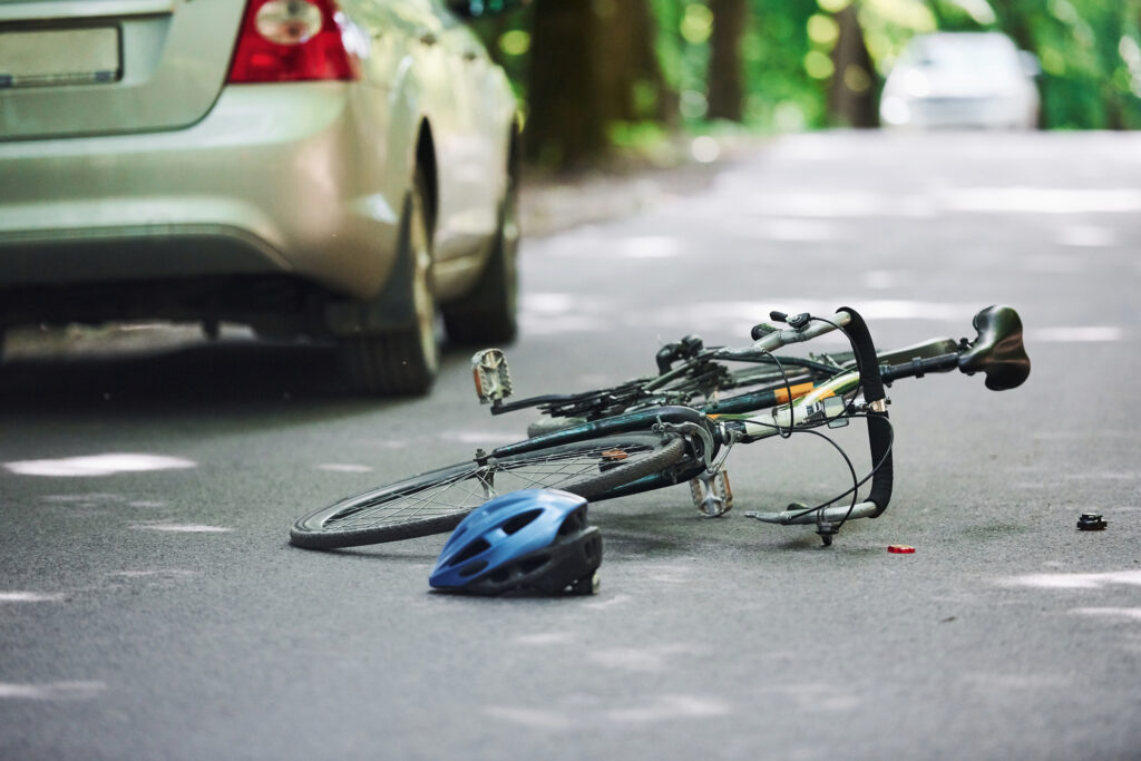 Bicycle and silver colored car accident on the road at forest at daytime.