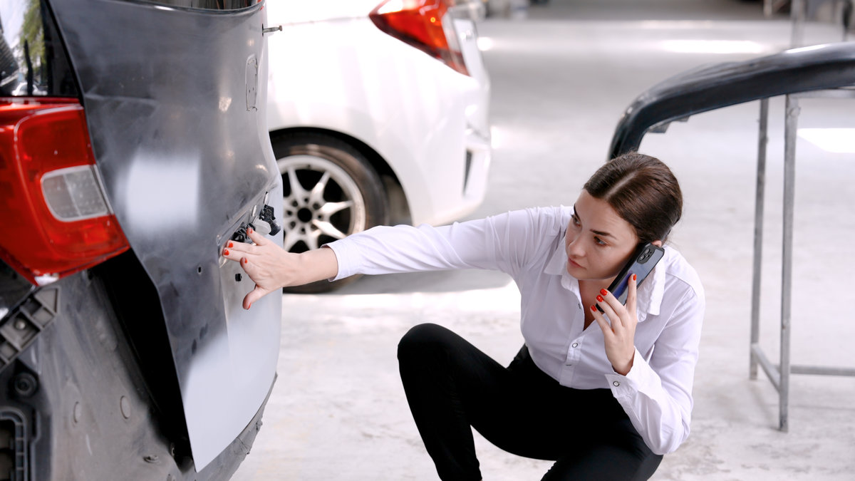 Caucasian woman using a mobile phone to call an insurance claim in an accident where the car was rear-ended to explain the damage to the car in order to prepare for repairs. in the auto repair shop